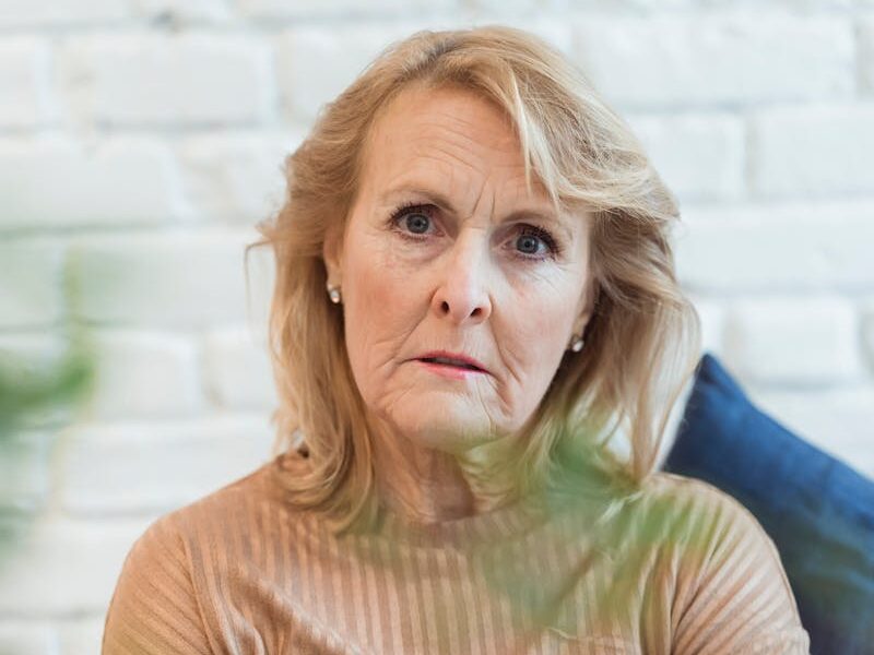Serious elderly female in clothes with striped ornament looking at camera while sitting on sofa at home