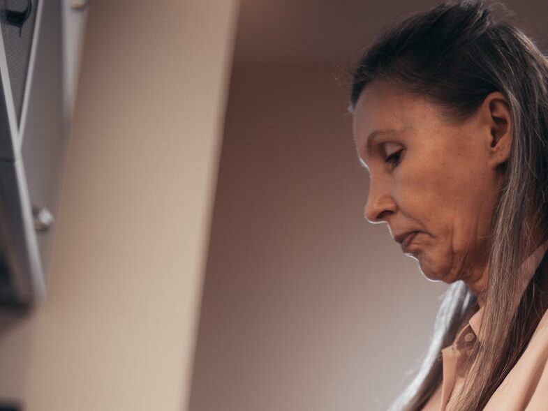 Elderly woman chopping vegetables on a cutting board in her kitchen, focused on cooking.