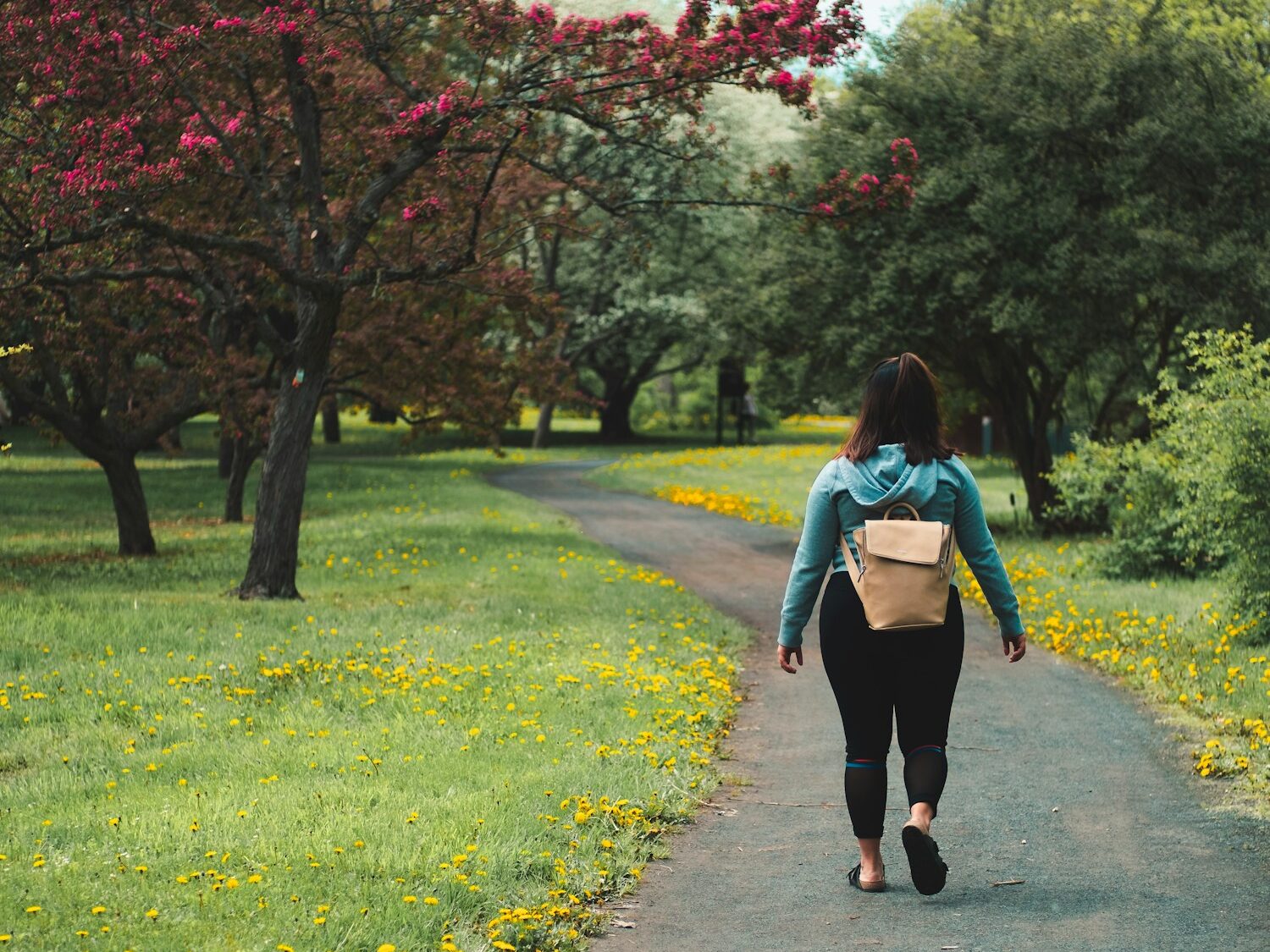 woman wearing blue jacket and black pants walking on grass field pathway