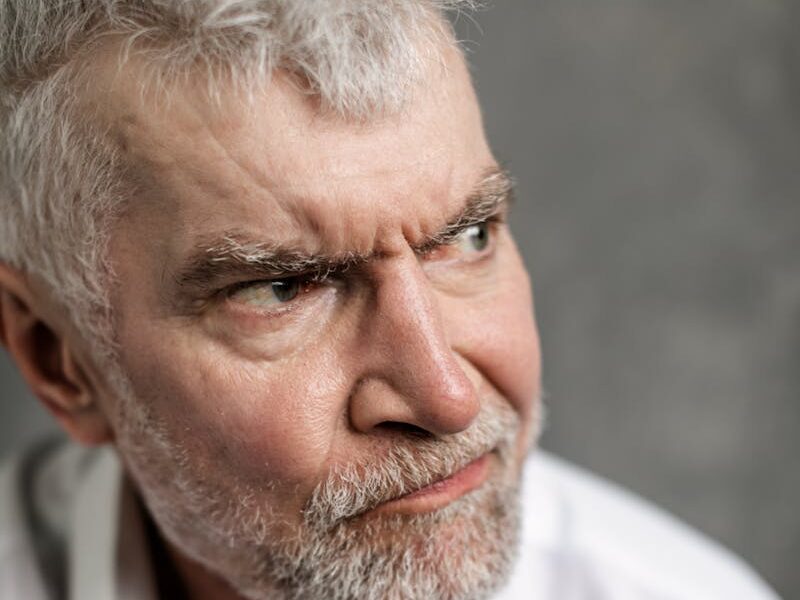 Portrait of a senior man with grey hair, looking pensive and serious, dressed in white shirt.