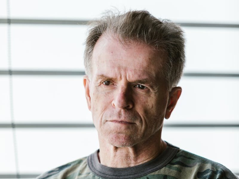 Close-up portrait of a senior military veteran wearing a camouflage shirt indoors.