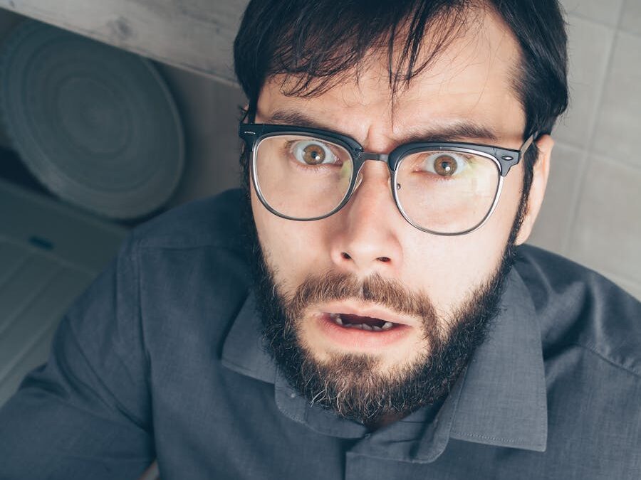 Astonished man wearing glasses holding paperwork indoors.