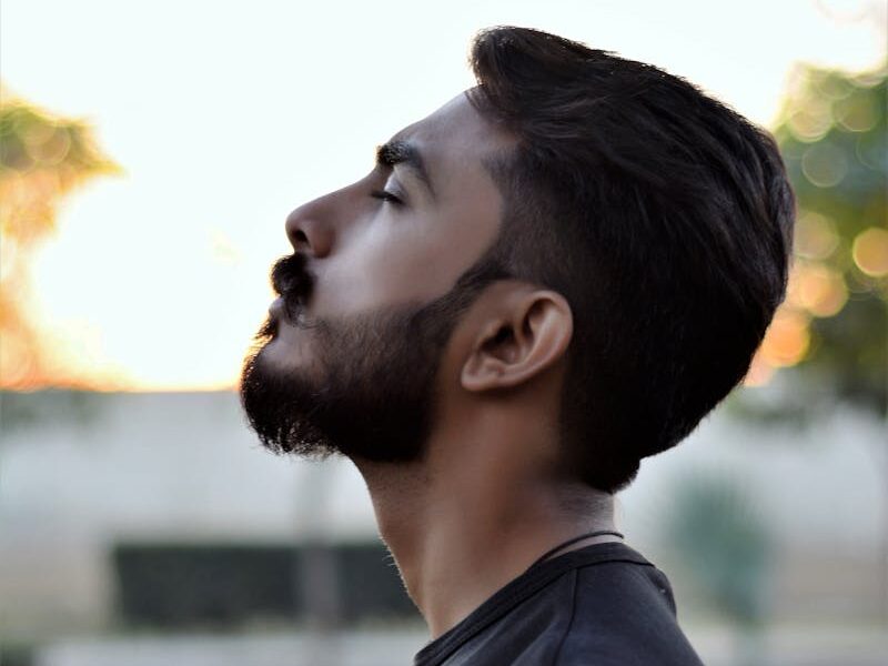 Side view portrait of a bearded man gazing upwards in an outdoor setting with blurred background.