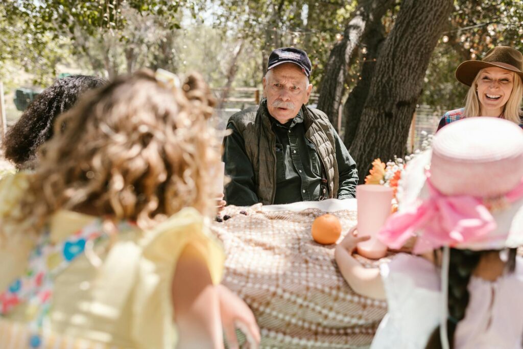 A family enjoys a sunny outdoor gathering, seated around a table with laughter and conversation.