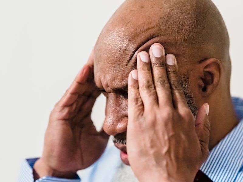 Adult bald man in shirt and tie holding head in stress, showing frustration.