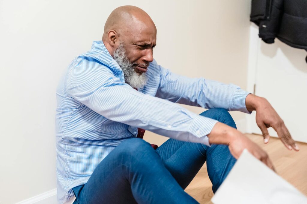 An emotional adult man sitting on a wooden floor, expressing vulnerability.
