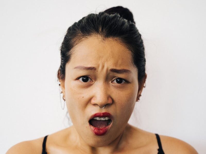A woman in a black top looks surprised, showcasing a shocked expression with her hand on her chest.