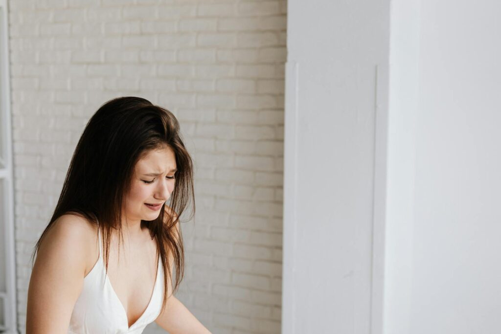 Young woman in white tank top experiencing intense emotion indoors.