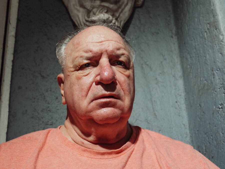 Senior man sitting against a blue wall with a stone sculpture overhead.