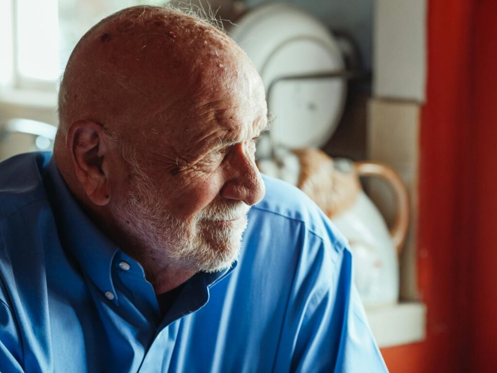 Portrait of a senior man wearing a blue shirt and beard, captured in a cozy indoor setting.