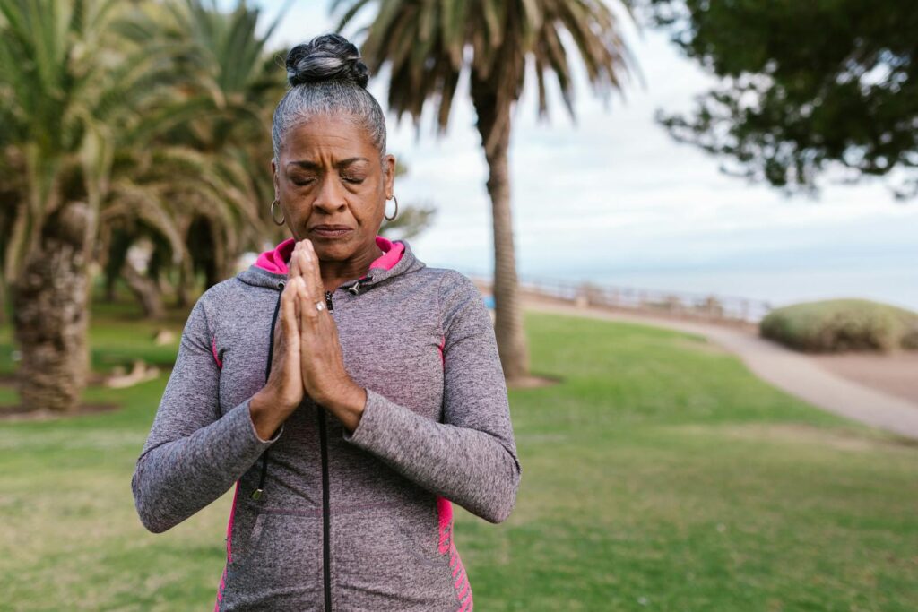 Elderly woman meditating outdoors in a park, promoting health and relaxation.