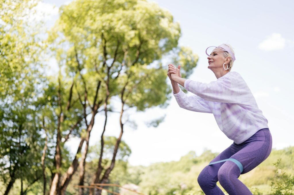 A senior woman exercises in a park with a resistance band, embracing a healthy lifestyle.