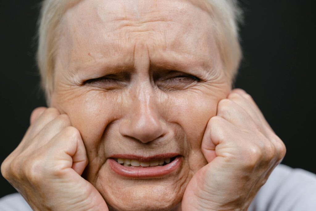Close-up of a distressed elderly woman expressing deep emotion with hands on face.