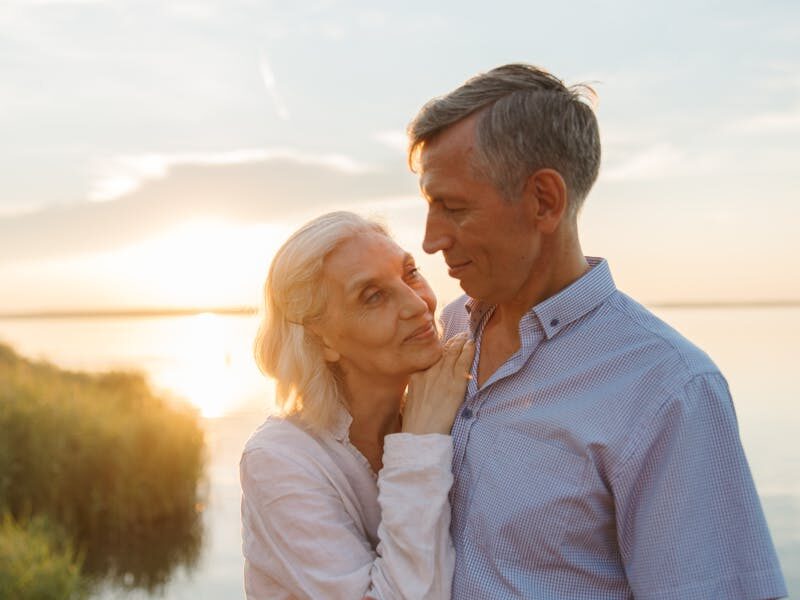 Elderly couple shares a tender moment by a lake during sunset, capturing love and serenity.