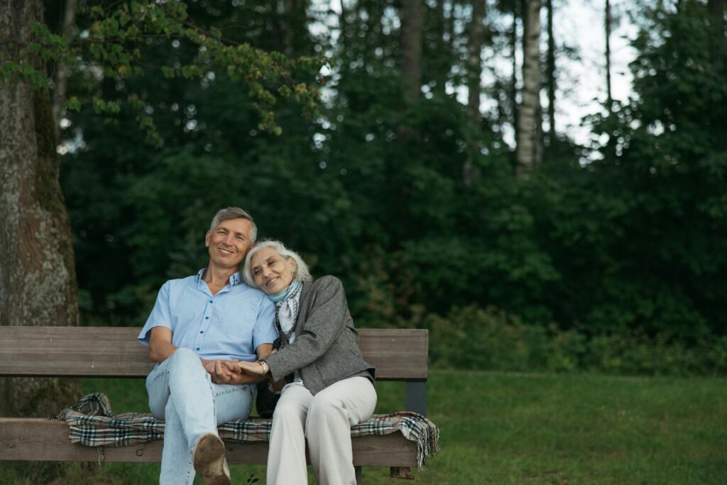 Elderly couple sitting on a bench, sharing a tender moment in a lush green park.