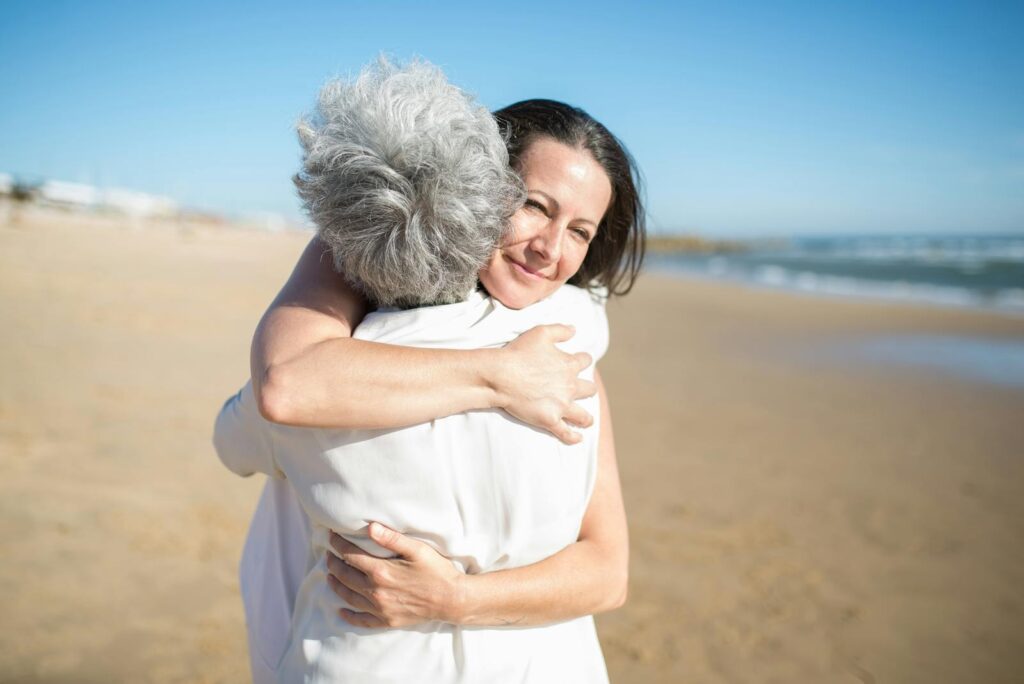 Mother and daughter hugging warmly on a sunny beach in Portugal.