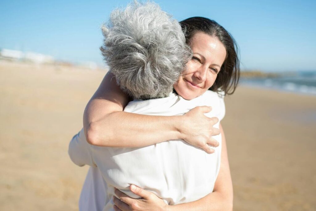 Mother and daughter hugging warmly on a sunny beach in Portugal.