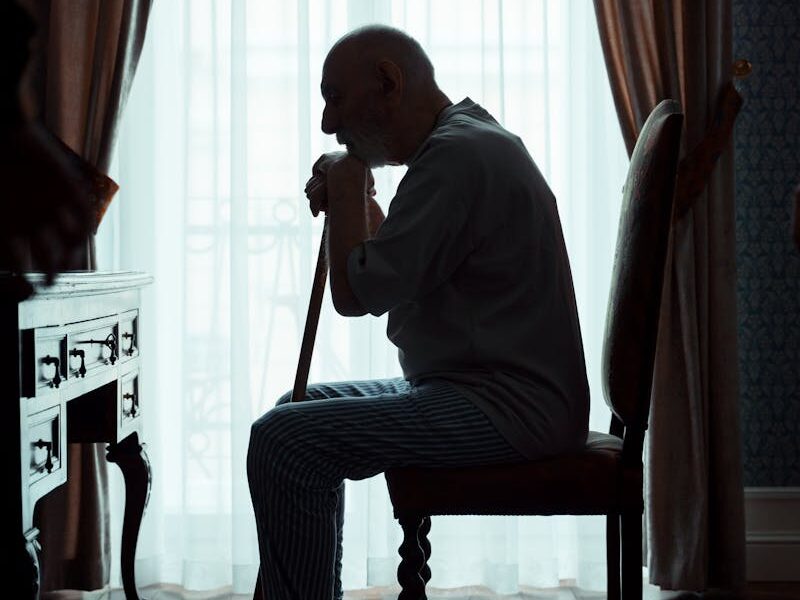 Silhouette of an elderly man sitting in a chair indoors, reflecting in a calm setting.
