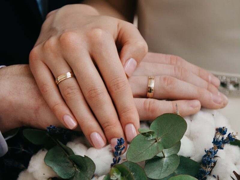 Close-up of couple's hands with gold wedding bands over a floral bouquet.