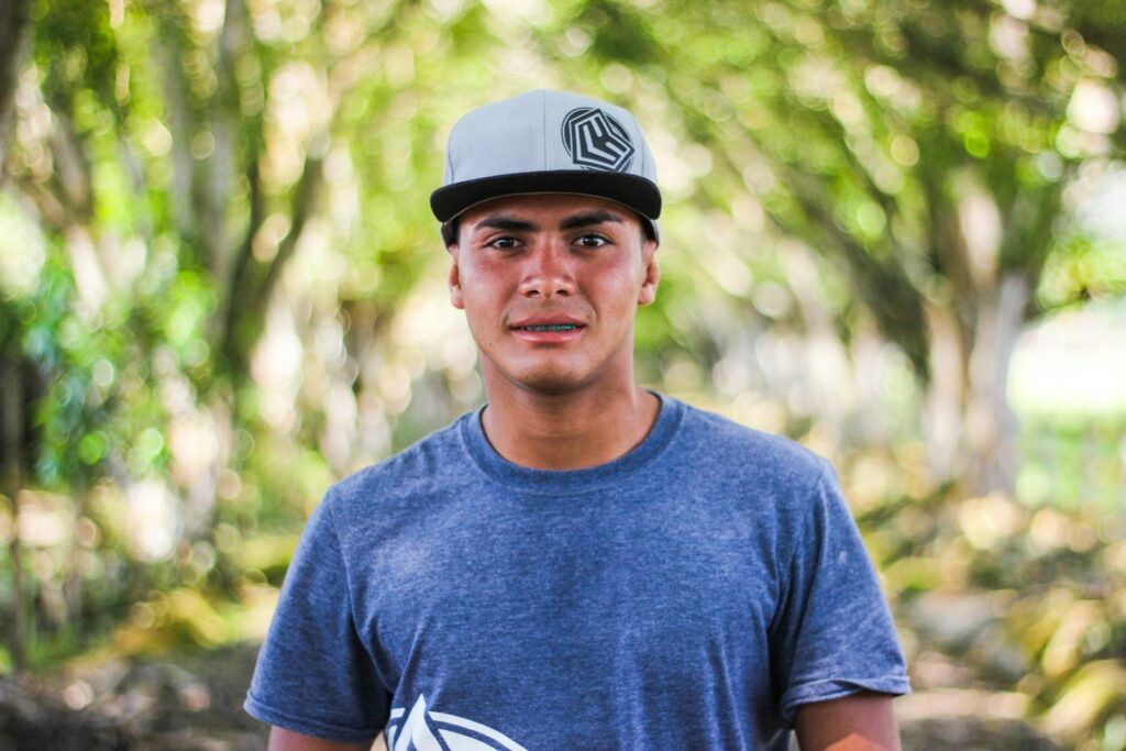 Portrait of a young man wearing a cap outdoors with a blurred natural background.