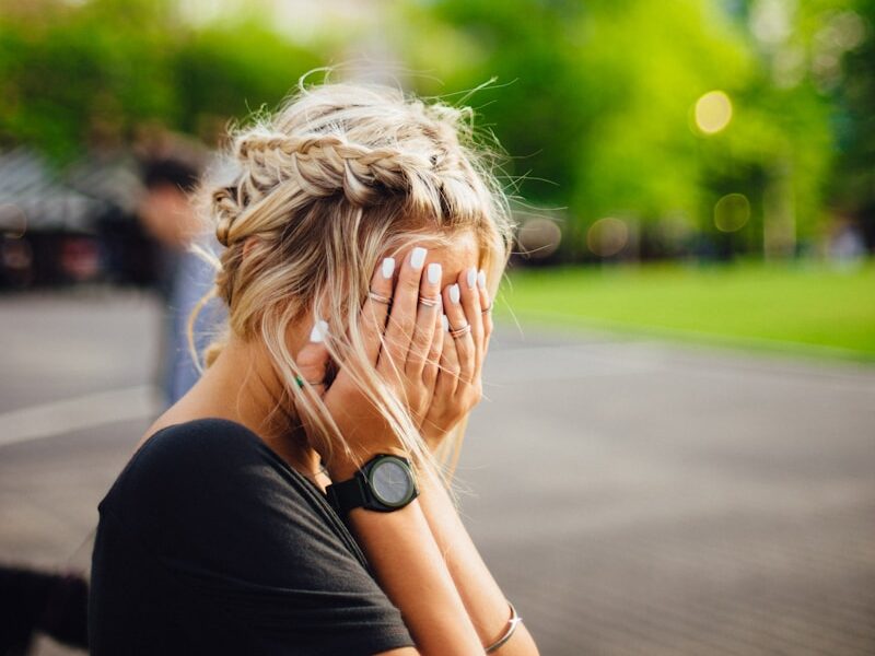 person covering face with hands outdoors