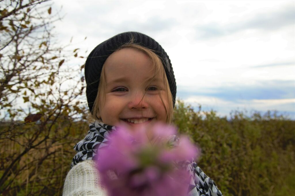 girl in white knit sweater holding pink flower during daytime