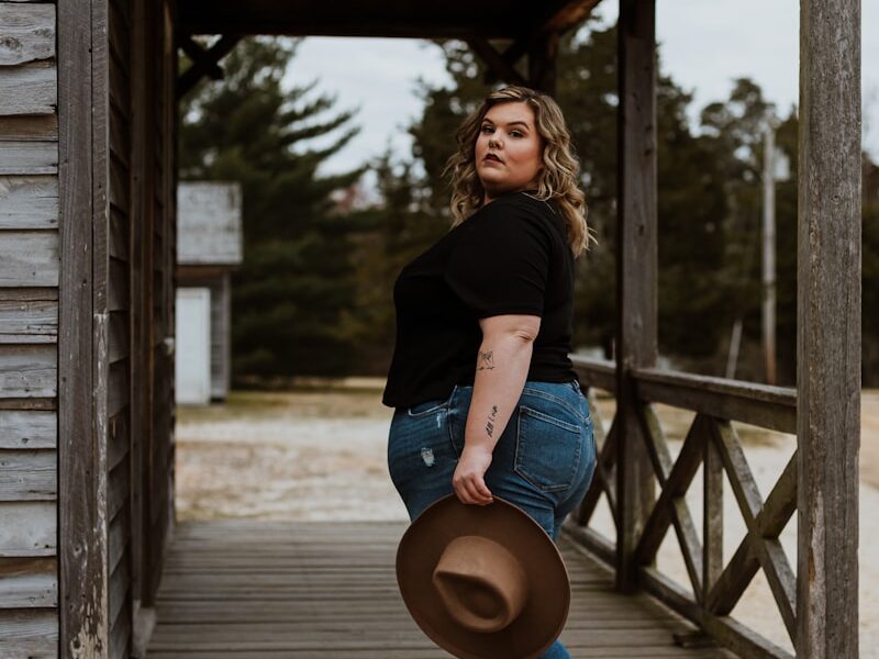 woman in black t-shirt and blue denim jeans holding brown hat