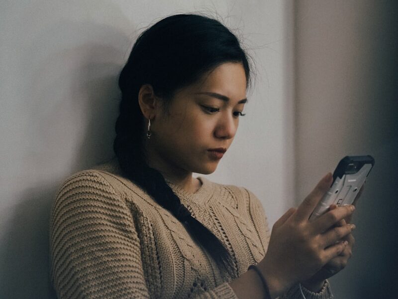 woman leaning back on white wall and using smartphone