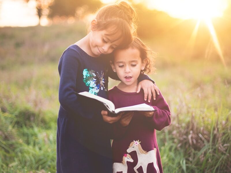 girl's left hand wrap around toddler while reading book during golden hour