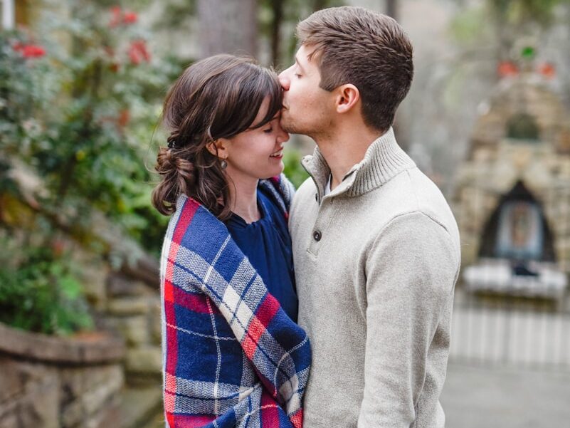 man kissing on woman forehead standing near tree during daytime