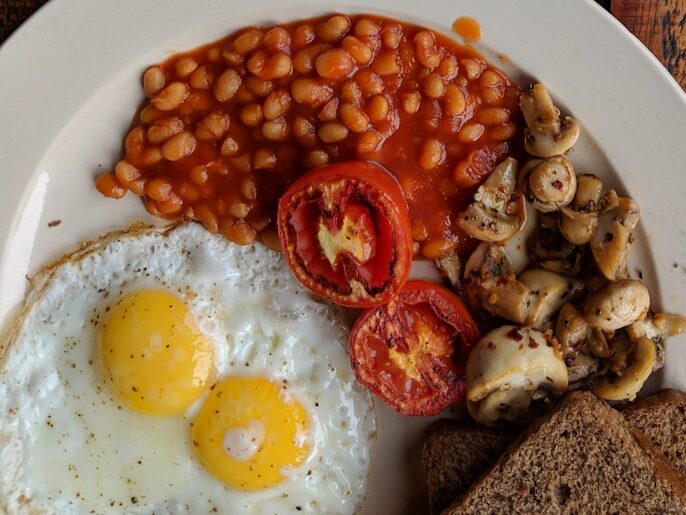 black coffee near sunny side up egg with sliced tomatoes, mushroom and bread on plate