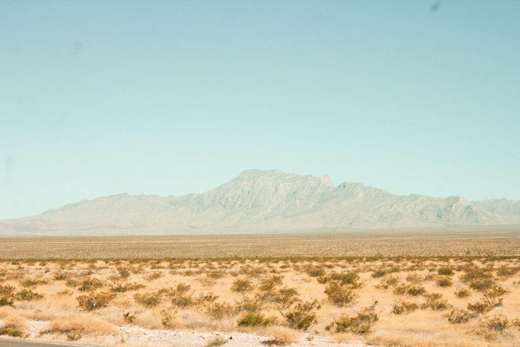 brown field near mountain under blue sky during daytime