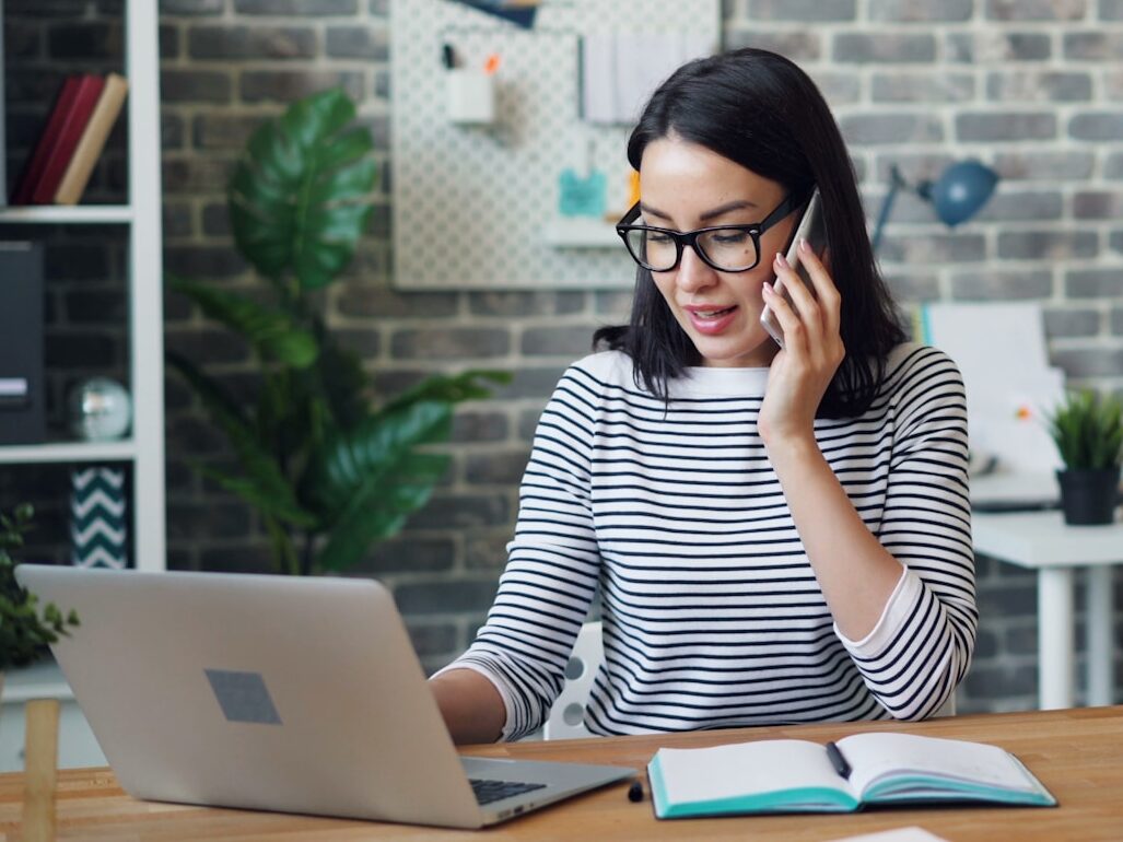 a woman talking on a cell phone while using a laptop