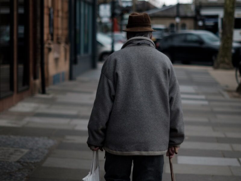 man walking using brown cane carrying white bag near brown buildings at daytime