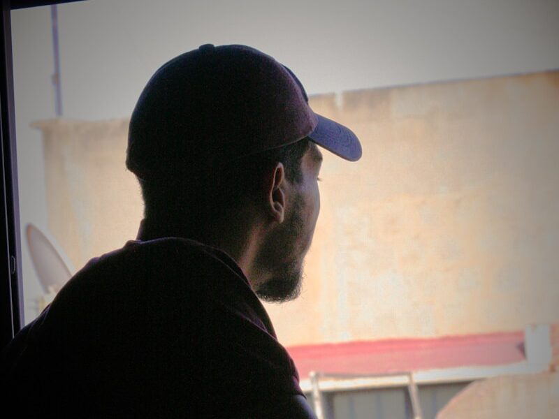 a man sitting in front of a window with a hat on