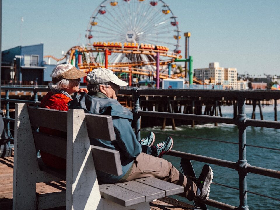 couple sitting on wooden bench near body of water during daytime