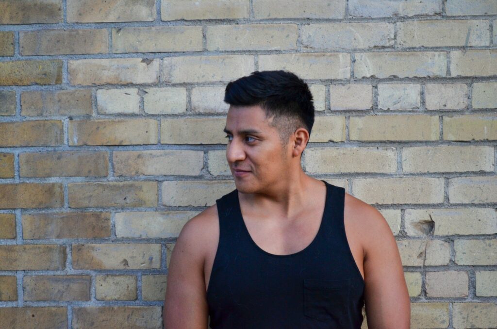 man in black tank top standing beside brick wall