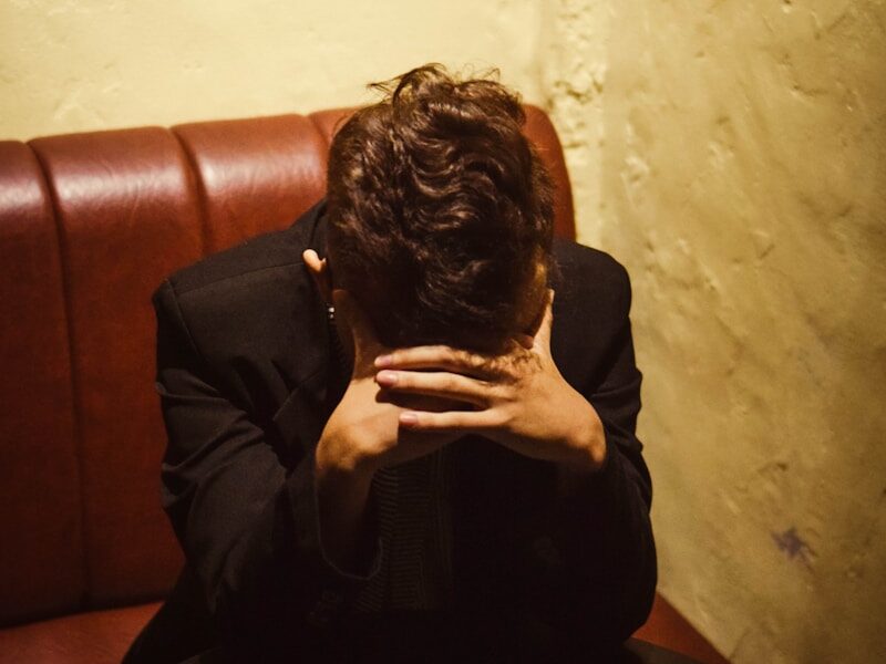 man sitting on red leather sofa beside white concrete wall