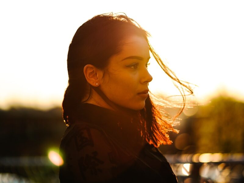 woman standing in front of gray metal fence during sunset