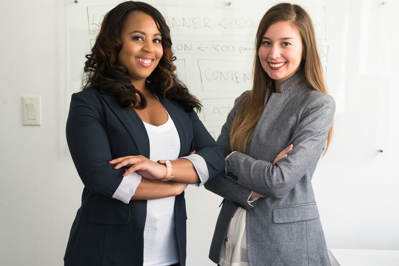 two women in suits standing beside wall