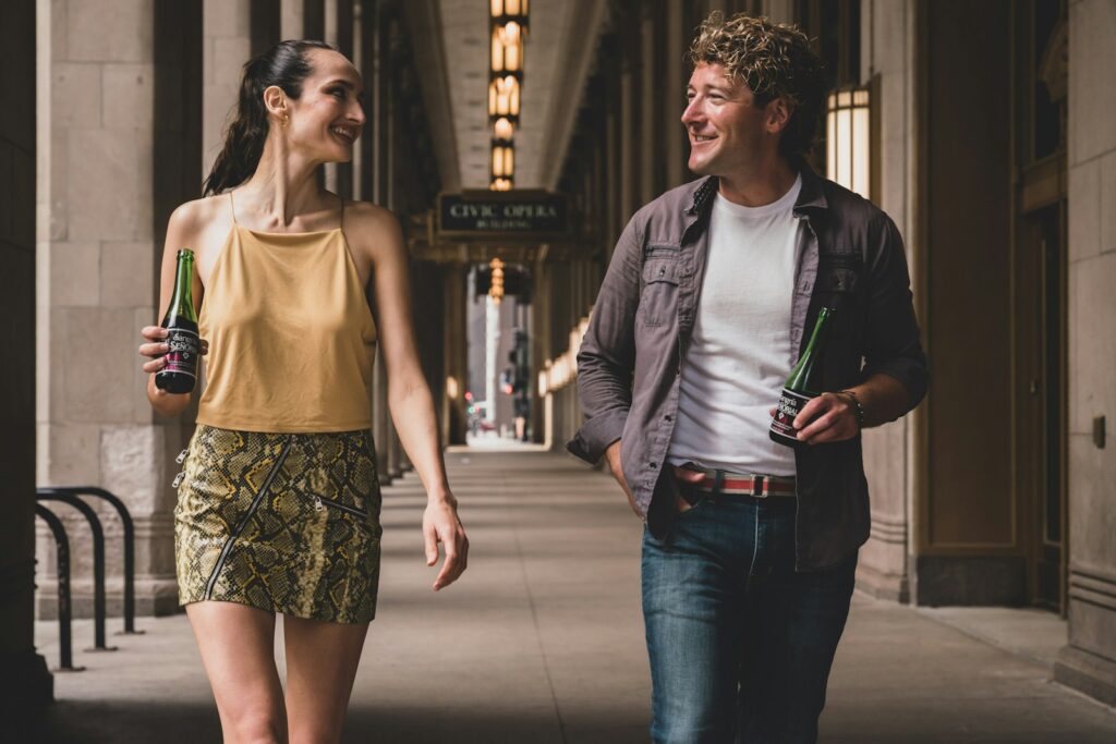 man in white tank top and black jacket standing beside woman in white tank top