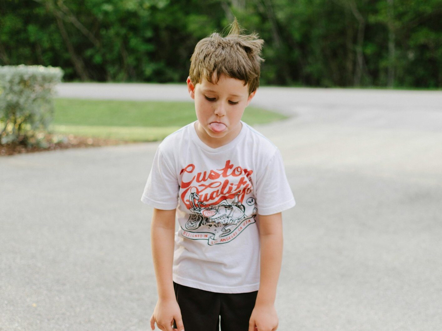 boy standing on gray concrete road while tongue out