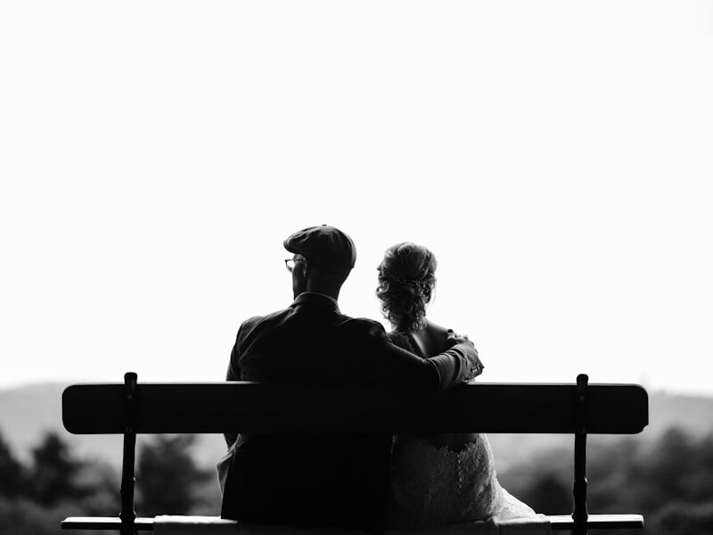 couple sitting on bench under tree grayscale photography