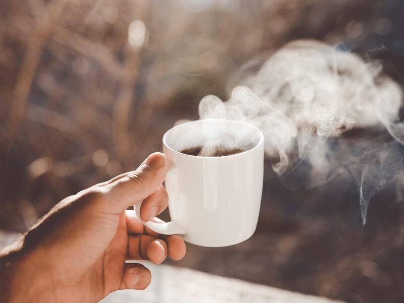 person holding white ceramic cup with hot coffee