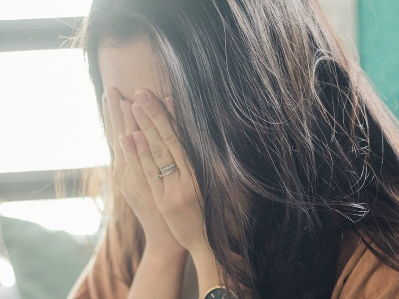 woman in brown shirt covering her face