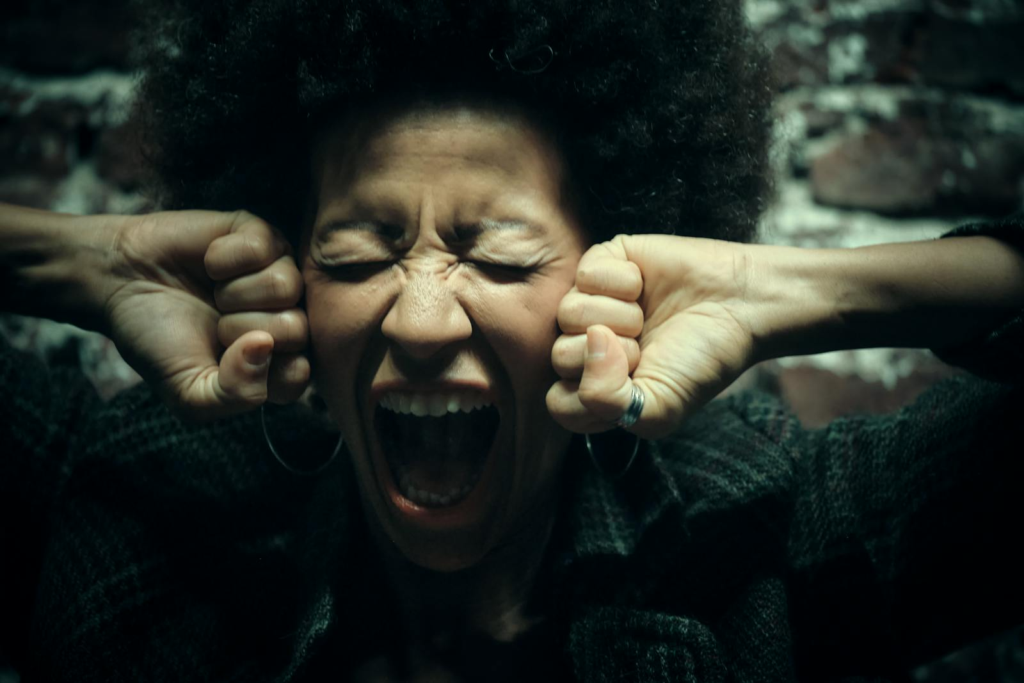 Close-up of a woman with afro hairstyle yelling with intense emotion against a brickwall.
