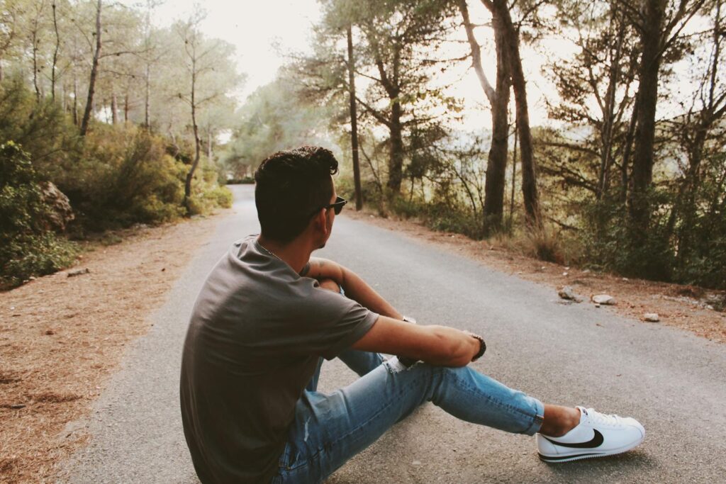 A young man sits on a forest road, enjoying solitude and nature's tranquility.