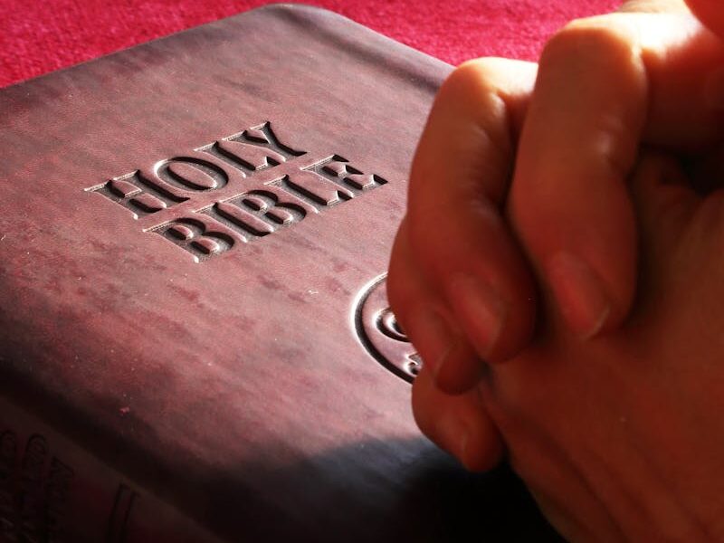 Close-up of hands praying on a Holy Bible, symbolizing faith and spirituality.