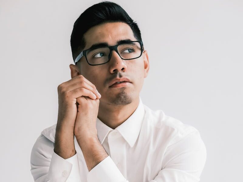 Portrait of a man wearing glasses and a white shirt, seated backward on a chair in a studio.