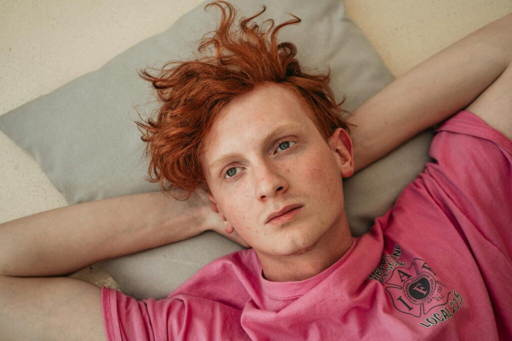 Close-up portrait of a man with red hair laying on a pillow indoors.